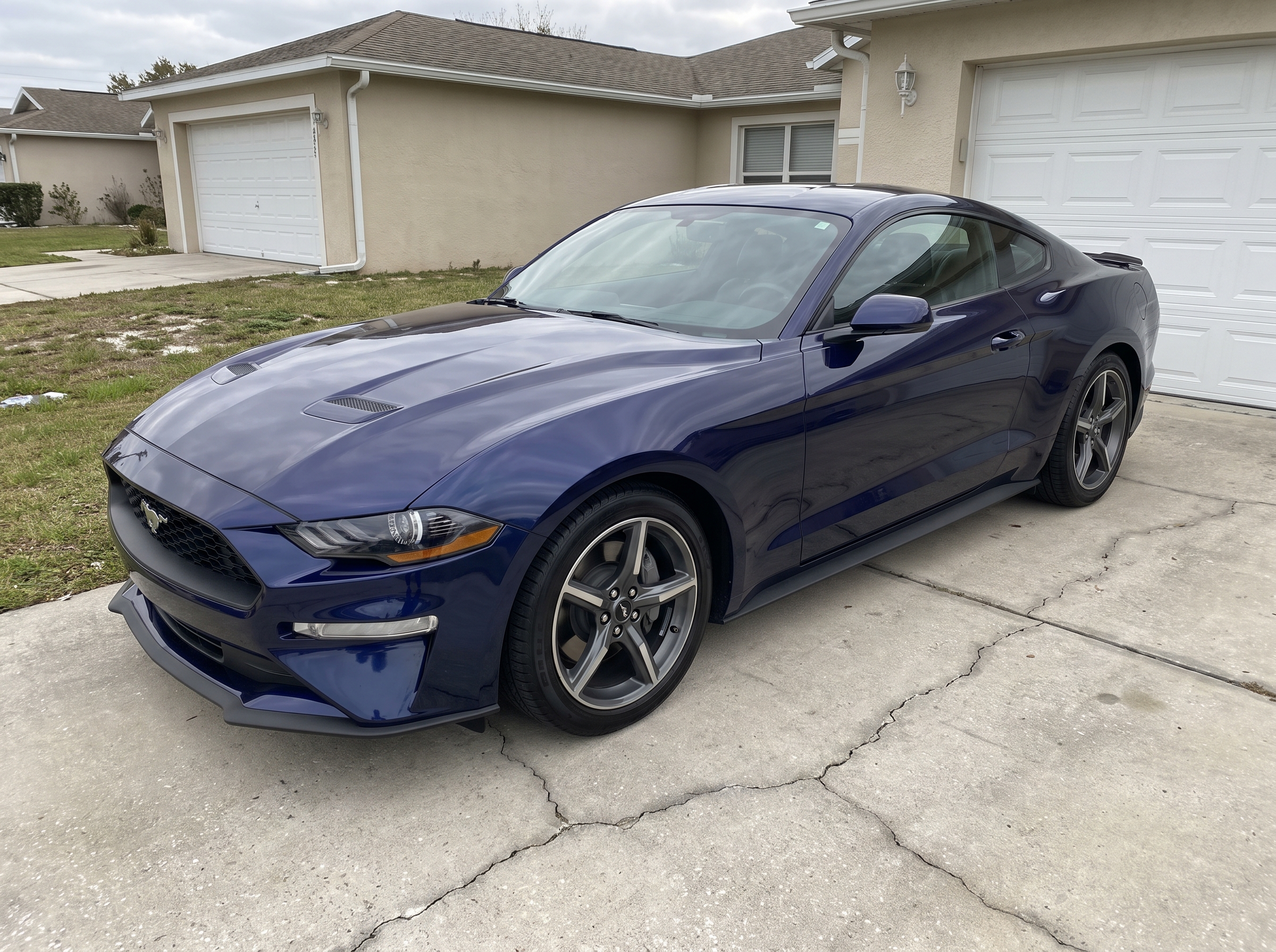 A navy blue coupe parked on a suburban driveway on an overcast afternoon